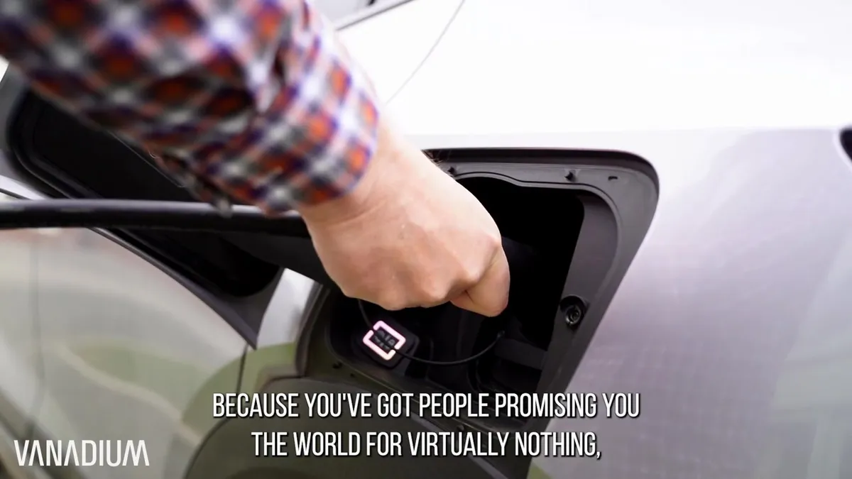 Close-up of a hand plugging a charging cable into an electric car's charging port.