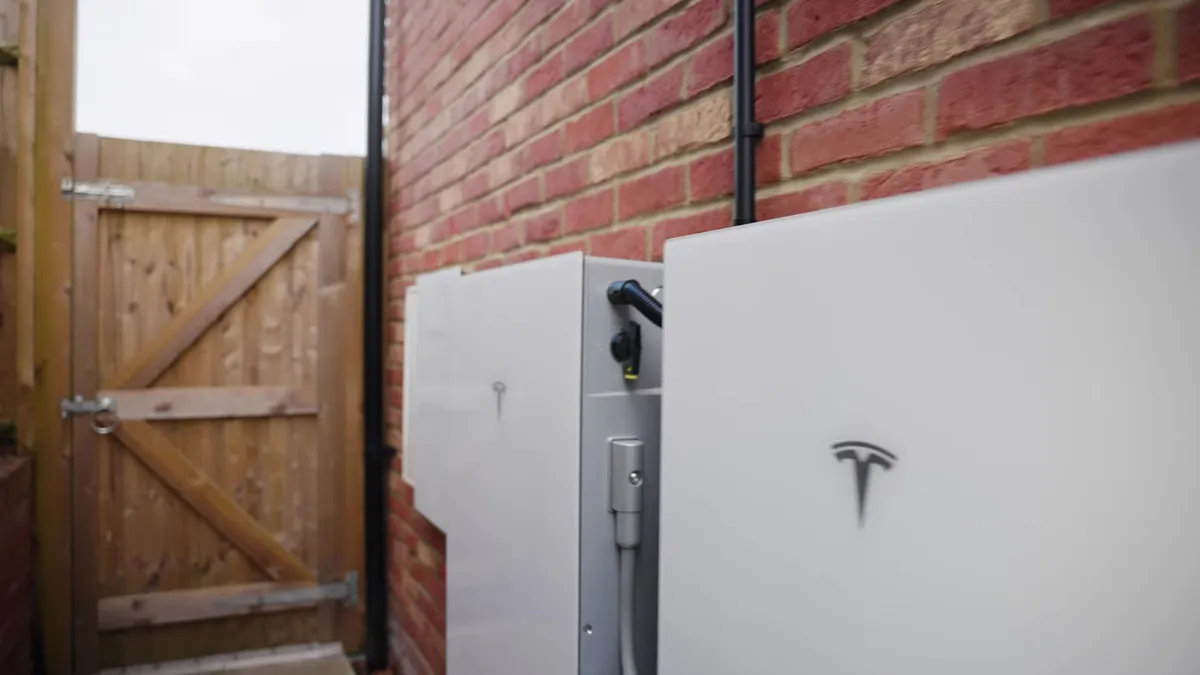 Three white Tesla Powerwall units mounted on the exterior brick wall of a house.