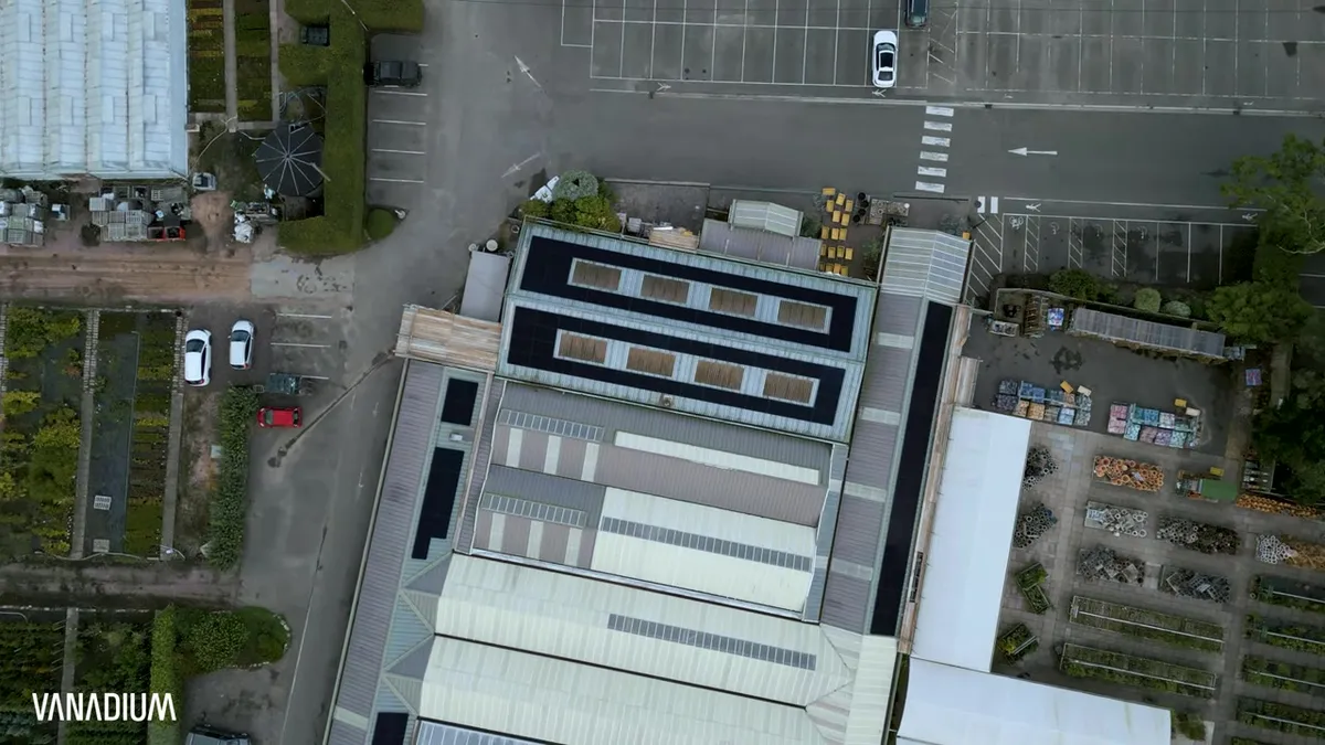 An aerial view shows solar panels on a commercial building next to a car park.