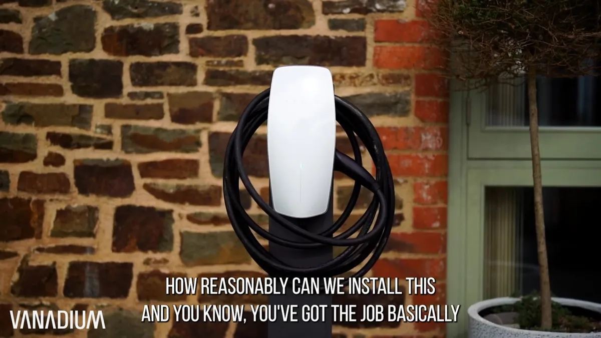 White Tesla Wall Connector EV charger with its cable neatly coiled around the unit, mounted on a stand.