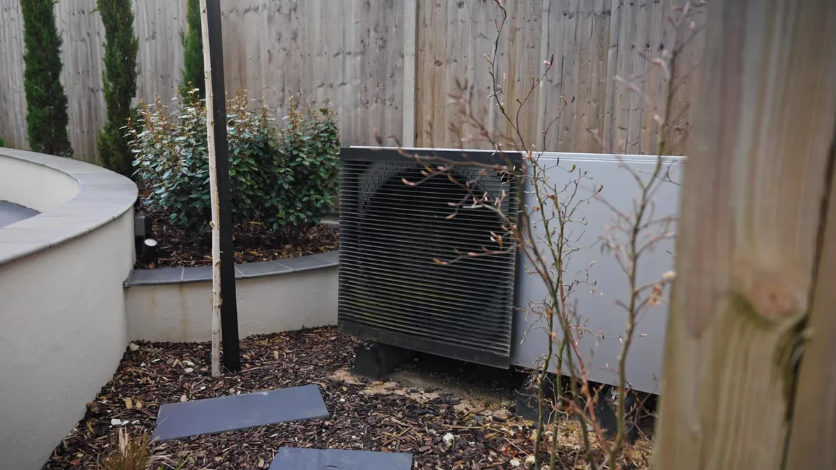 An outdoor air source heat pump unit next to a brick wall.
