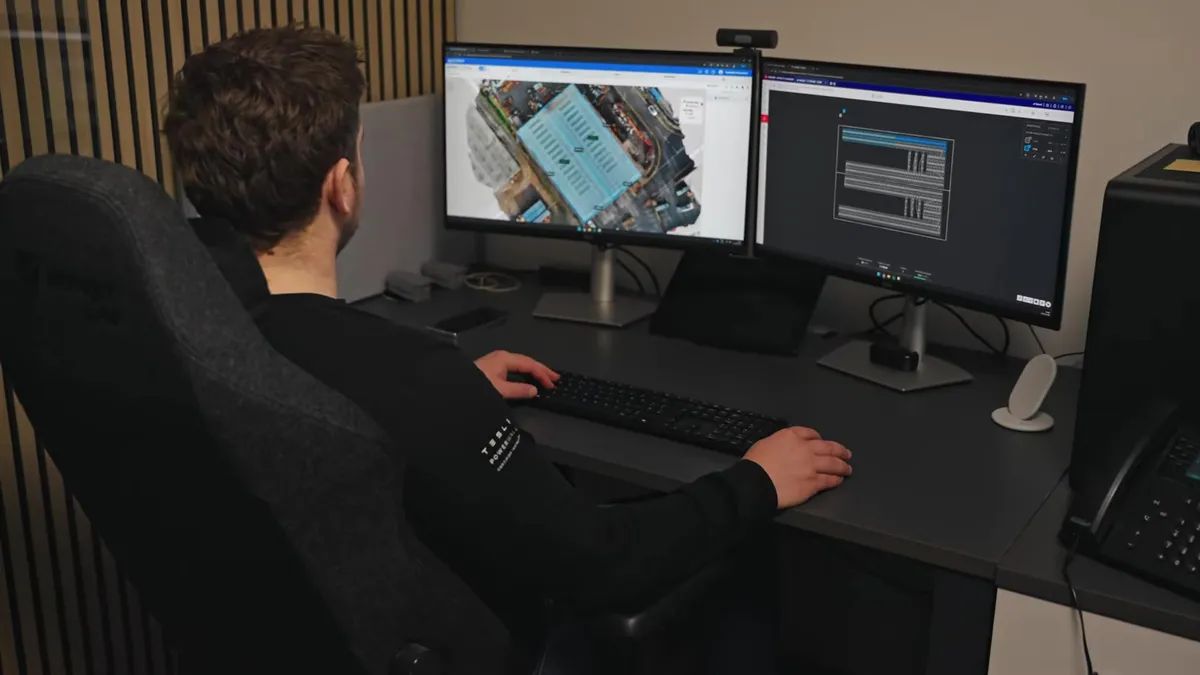 An engineer works at a desk with two monitors displaying solar panel designs.