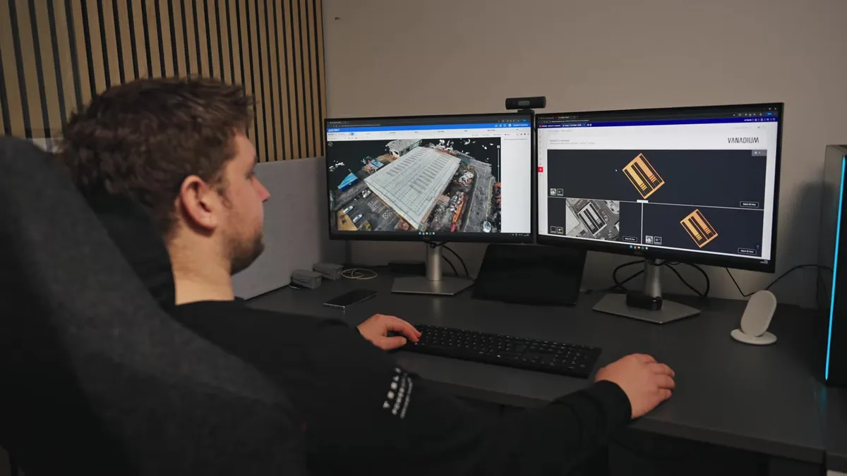 An engineer works at a desk with two monitors displaying solar panel data.