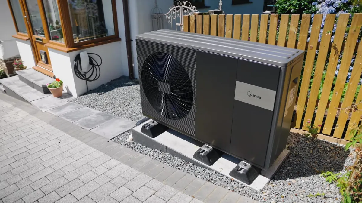 A heat pump is installed outside a house next to a wooden fence.