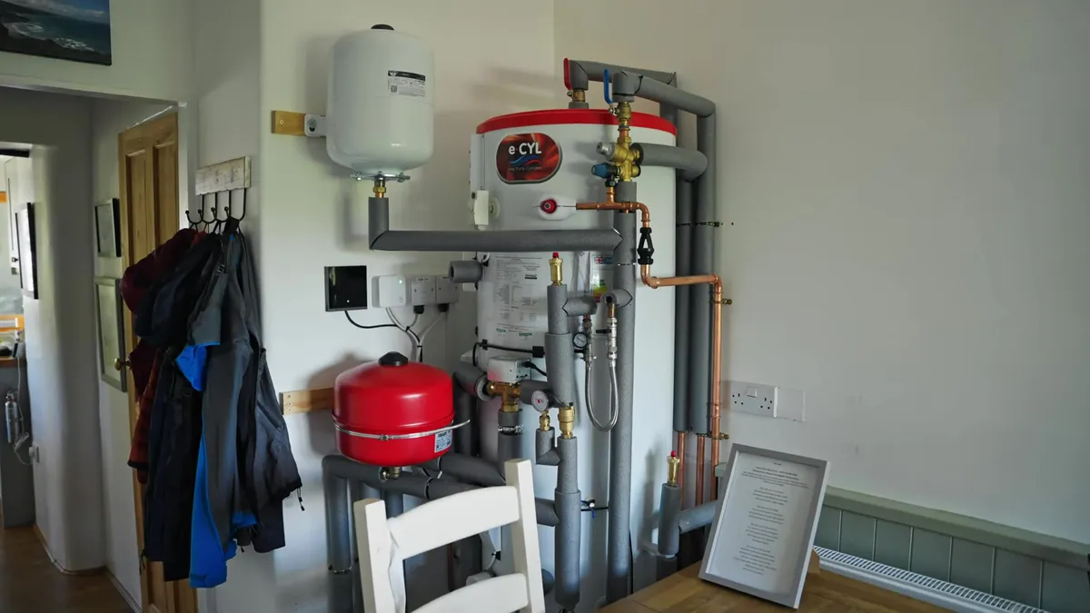A heat pump cylinder and associated pipework are visible in a domestic setting.
