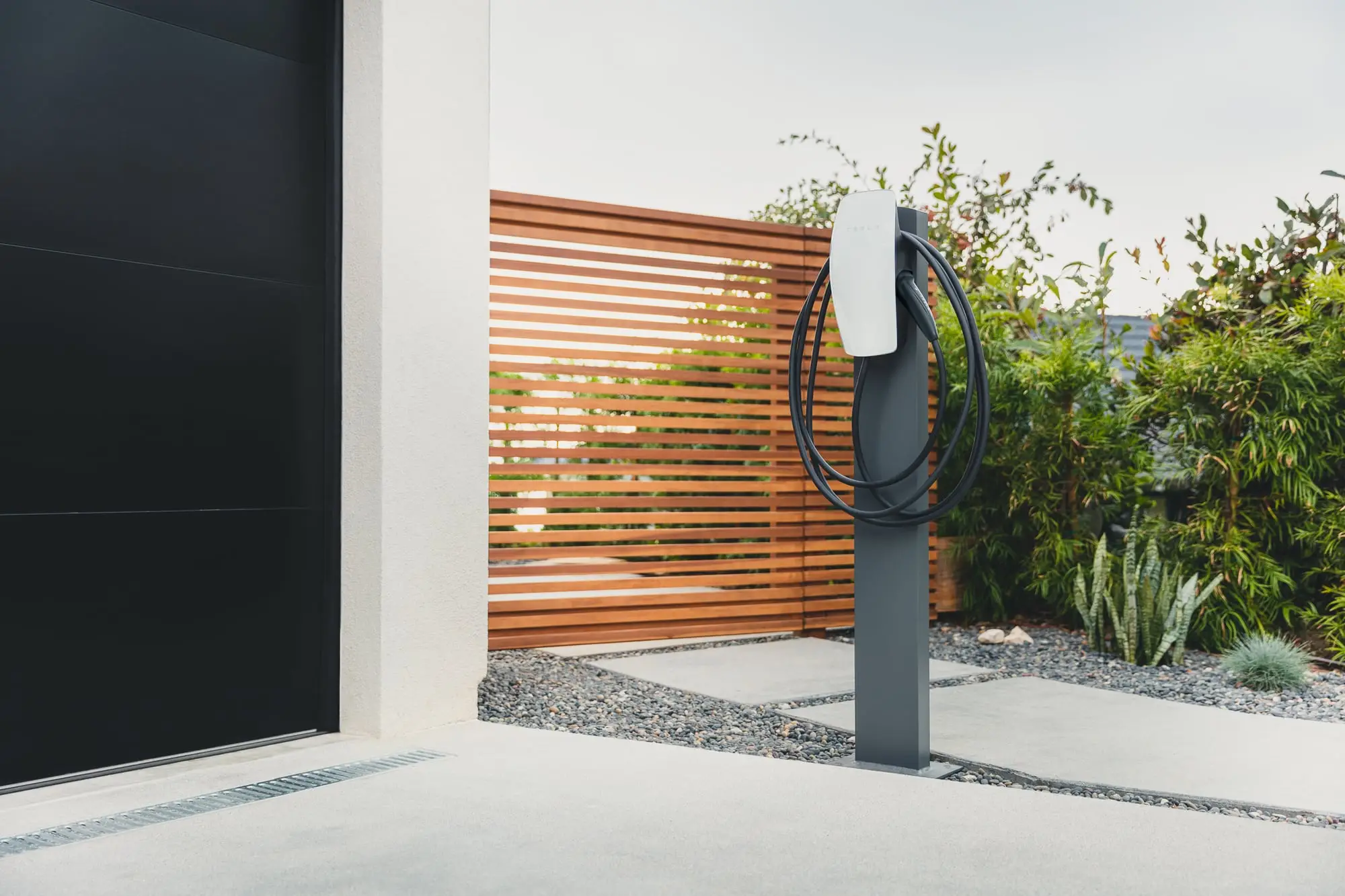 Tesla Wall Connector on a pedestal beside a garage door